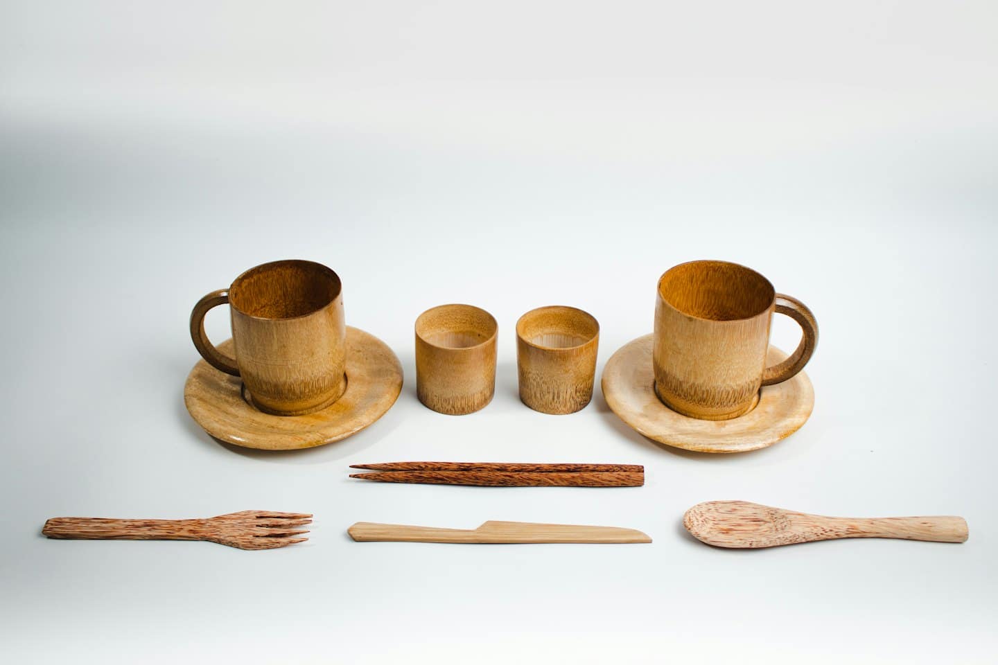 Wooden kitchen utensils and cups arranged neatly on white.