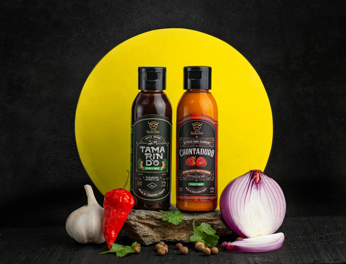 Two hot sauce bottles surrounded by fresh ingredients on wood.