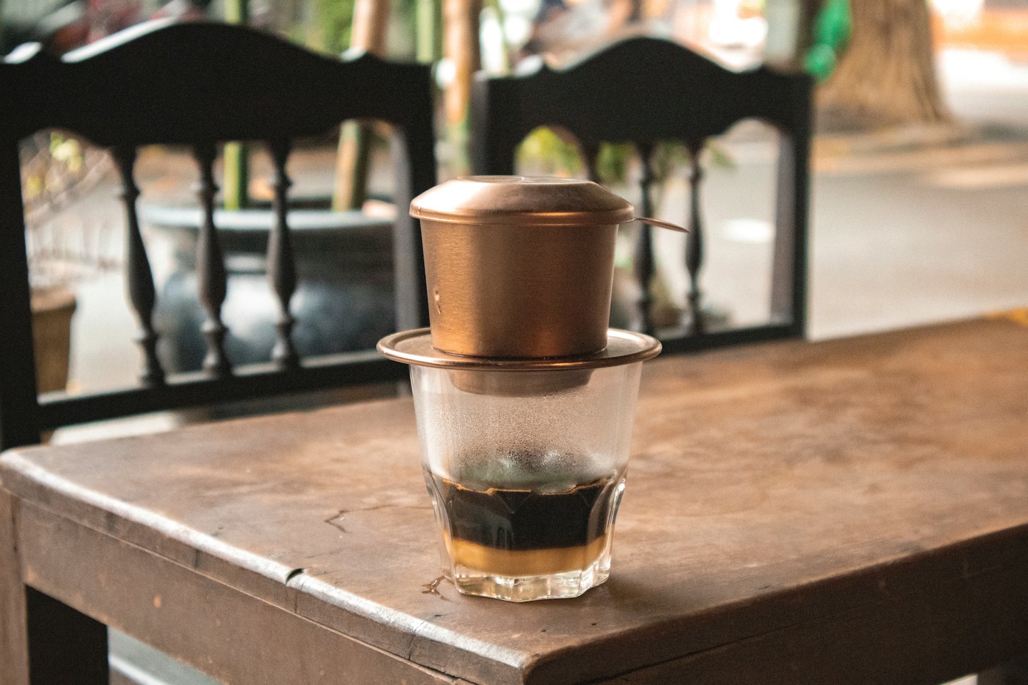 Vietnamese coffee drips from a metal filter into a glass.