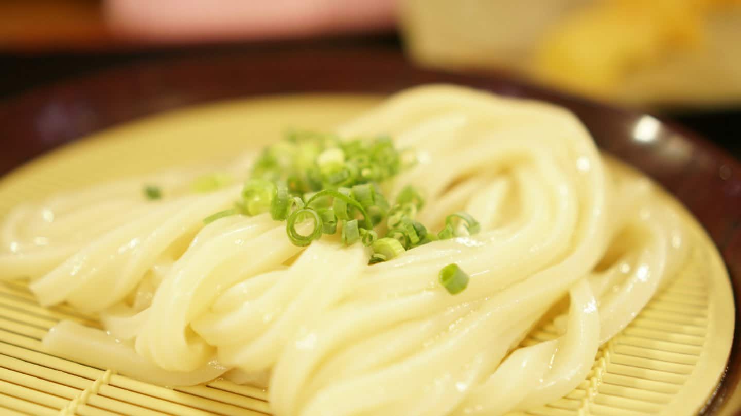 Glossy udon noodles with green onions sit on a bamboo mat.